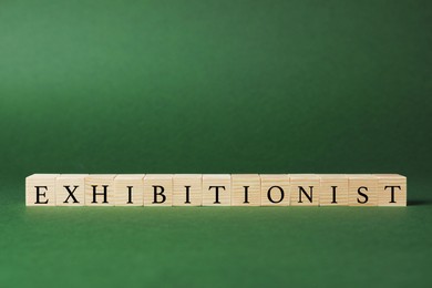 Word EXHIBITIONIST made with wooden cubes on dark green background