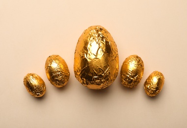 Chocolate eggs wrapped in golden foil on beige background, flat lay