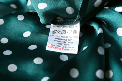 Clothing label with care instructions and content information on green polka dot garment, closeup
