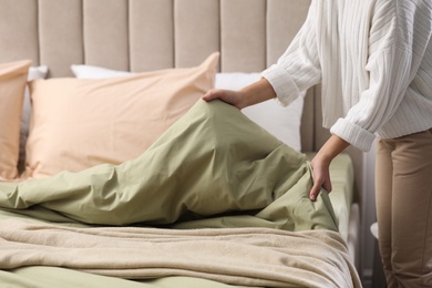 Woman making bed with new pistachio linen in room, closeup