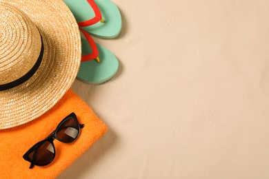 Beach towel, sunglasses, hat and flip flops on sand, flat lay. Space for text