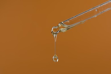 Dripping hydrophilic oil from pipette on brown background, closeup. Space for text