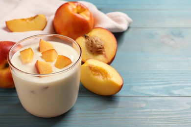 Tasty peach yogurt with pieces of fruit in glass on light blue wooden table, space for text