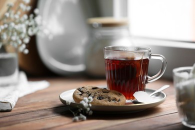 Cup of freshly brewed tea and delicious cookies on wooden table, space for text