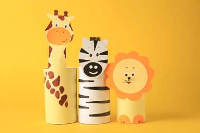 Photo of Toy giraffe, lion and zebra made from toilet paper hubs on yellow background. Children's handmade ideas