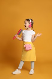 Cute little girl in headphones with brush singing on orange background