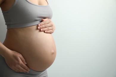Pregnant young woman touching belly on light background, closeup. Space for text