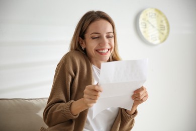 Excited woman reading letter on sofa at home