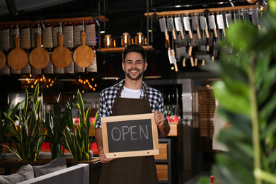 Young business owner holding sign OPEN in his cafe