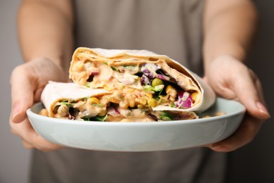 Photo of Woman holding plate with delicious hummus wraps, closeup