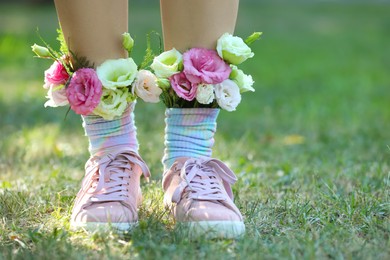 Woman standing on green grass with flowers in socks, closeup. Space for text