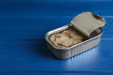 Photo of Open tin can of tasty cod liver on blue wooden table, closeup. Space for text