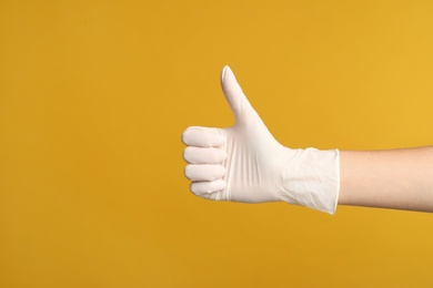 Doctor in medical gloves showing thumb up on yellow background, closeup. Space for text