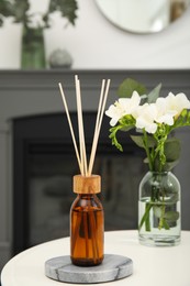 Reed diffuser and vase with bouquet on white table in room