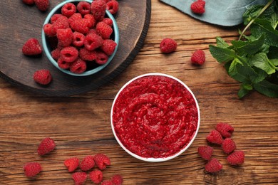 Photo of Raspberry puree in bowl and fresh berries on wooden table, flat lay