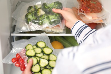 Photo of Woman putting vacuum bags with vegetables into fridge, closeup. Food storage