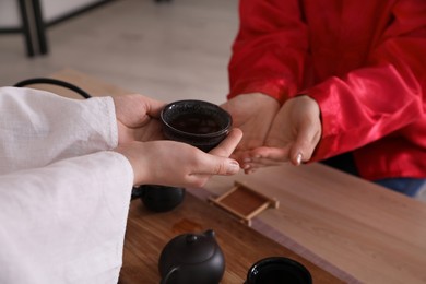 Master giving freshly brewed tea to guest during ceremony at table, closeup