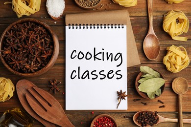 Notebook with inscription Cooking Classes, raw pasta and spices on wooden table, flat lay