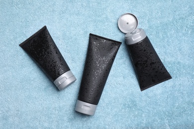 Black tubes with men's cosmetic products on light blue towel, flat lay