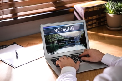 Man with laptop booking tickets online at wooden table, closeup. Travel agency concept