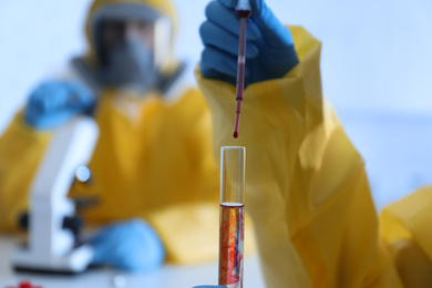 Scientist in chemical protective suit dripping blood  into test tube at laboratory, closeup. Virus research