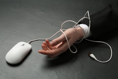 Photo of Man tied with computer mouse cable at black table, closeup. Internet addiction