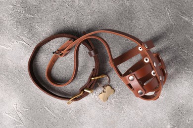 Photo of Brown leather dog muzzle and collar on light gray textured table, top view