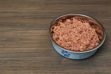 Wet pet food in feeding bowl on wooden background, space for text