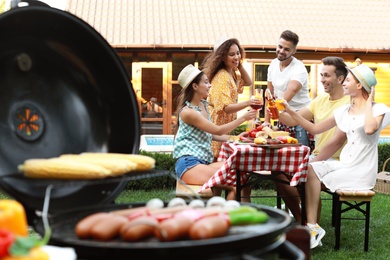 Photo of Group of friends at barbecue party outdoors. Blurred view of grill with sausages and vegetables