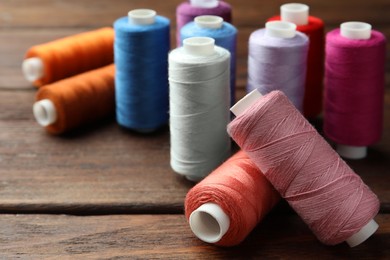 Different colorful sewing threads on wooden table, closeup. Space for text