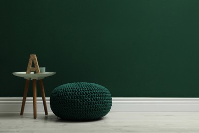 Photo of Stylish knitted pouf and table near green wall indoors, space for text