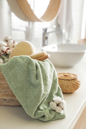 Wicker basket with clean towel, massage brush and cotton flowers on countertop in bathroom
