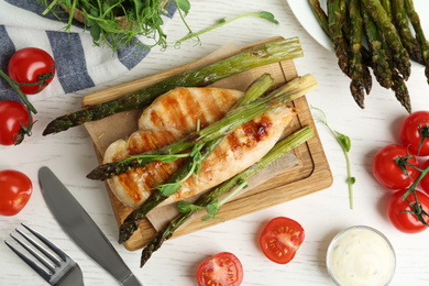 Tasty grilled chicken fillet served with asparagus and sprouts on white wooden table, flat lay