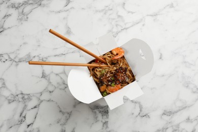 Box of wok noodles with seafood and chopsticks on white marble table, top view