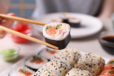 Woman holding tasty sushi roll with chopsticks at table, closeup