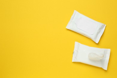 Wet wipes flow packs on yellow background, flat lay. Space for text 