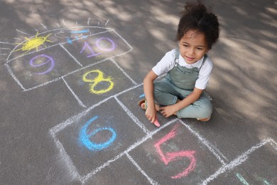 Little African American girl drawing hopscotch with chalk on asphalt outdoors. Happy childhood