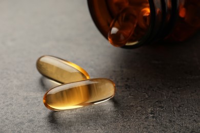 Overturned bottle with dietary supplement capsules on grey table, closeup