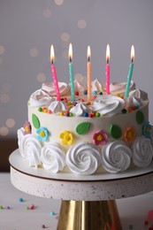Delicious birthday cake with party decor on stand against blurred festive lights, closeup
