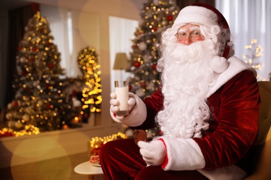 Santa Claus with glass of milk and cookie in room decorated for Christmas