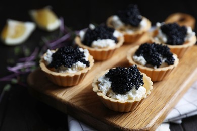 Photo of Board of delicious tartlets with black caviar and cream cheese on wooden table, closeup