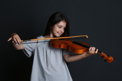 Preteen girl playing violin on black background