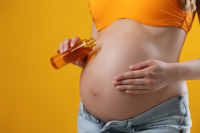 Young pregnant woman with sun protection oil on yellow background, closeup. Space for text