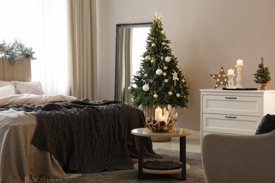 Beautiful decorated Christmas tree with fairy lights in bedroom interior