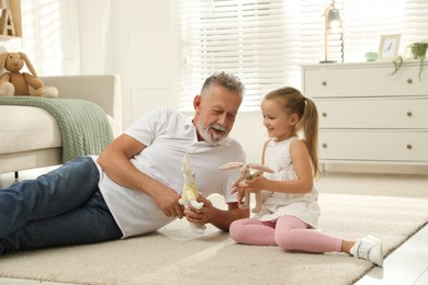 Happy grandfather and his granddaughter playing with toys together at home