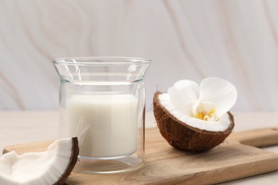 Photo of Glass of delicious vegan milk, coconut pieces and flower on white wooden table