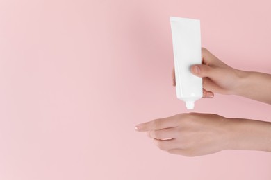 Woman applying cream onto hand on pink background, closeup. Space for text