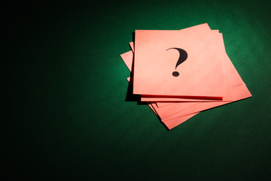 Pink paper cards with question mark on dark green background, above view. Space for text