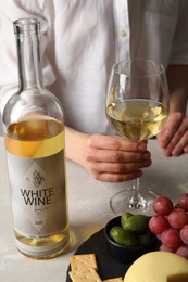 Photo of Woman holding glass of white wine at table with snacks, closeup