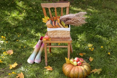 Rubber boots, chair, pumpkin and apples on green grass outdoors. Autumn atmosphere